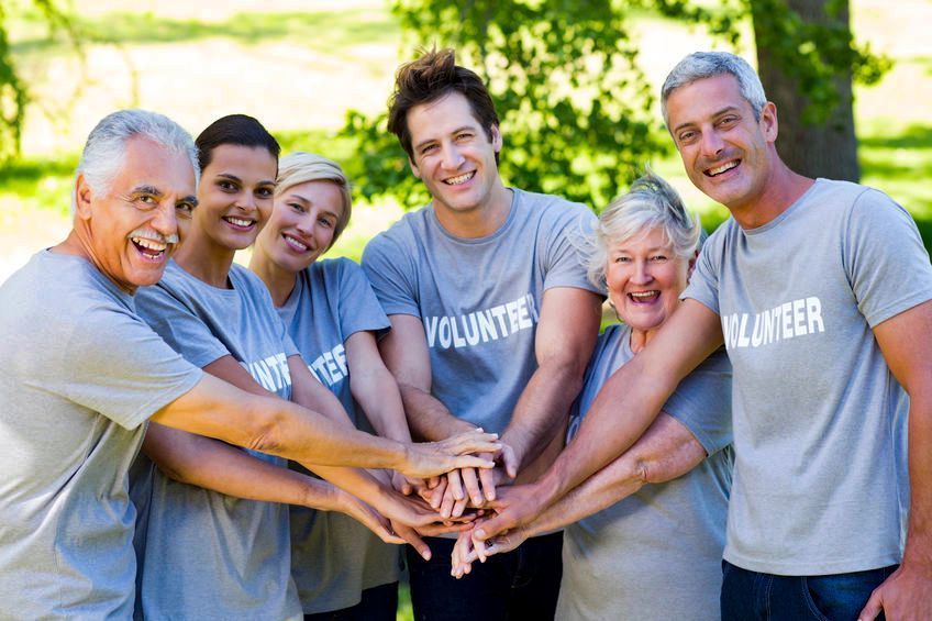 Group of diverse volunteers smiling with hands together in a park.