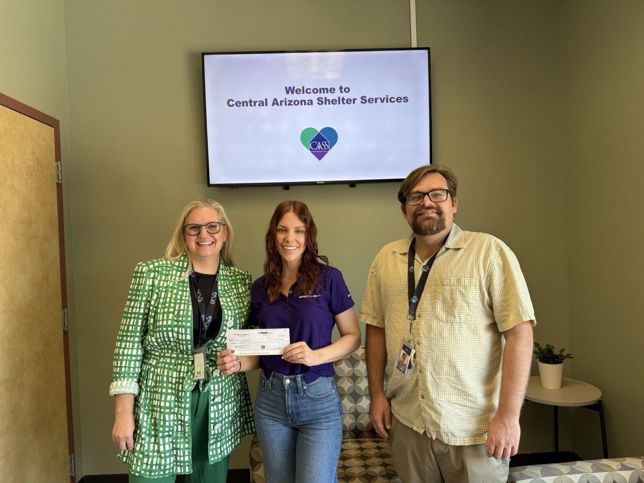 Three people at an animal shelter; two women and a man. Middle woman holds a check.