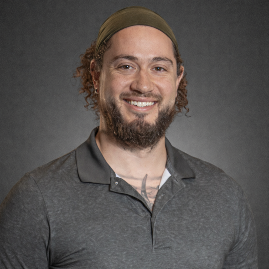 Man with curly hair and beard smiling, wearing a gray polo shirt and green headband.