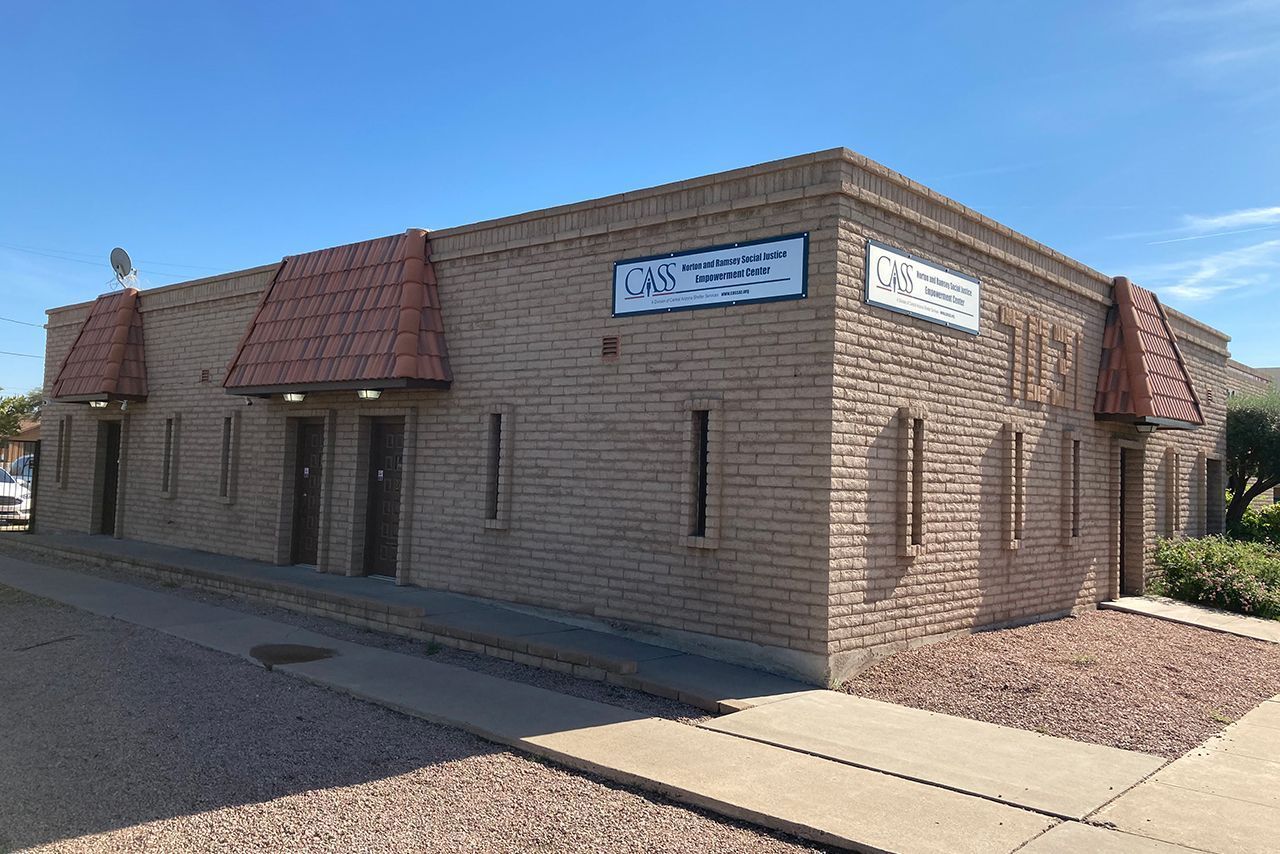 Tan brick building with red tiled awnings, two visible signs, and blue sky.