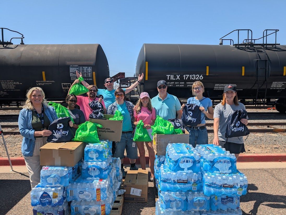 People stand with water bottles and donations in front of train cars to help.