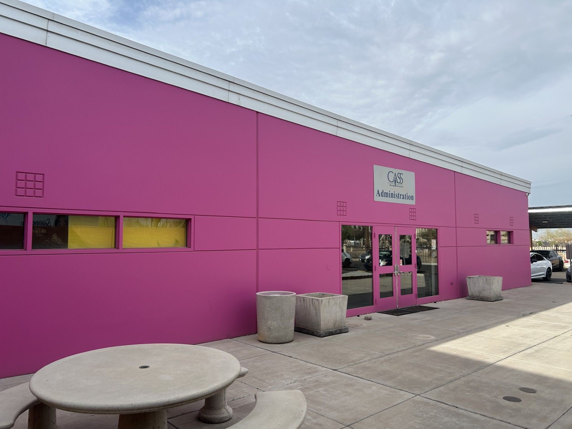 Bright pink building with white trim, gray concrete planters, and a table.