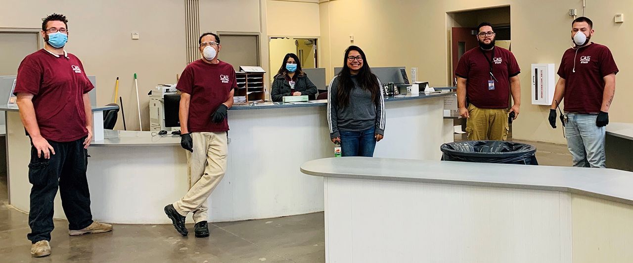 Staff behind a reception counter wearing masks and gloves. Two are leaning.