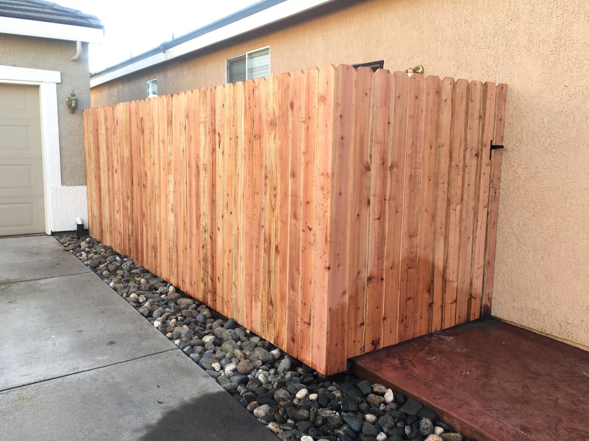A wooden fence is surrounded by rocks in front of a house.