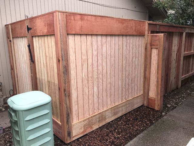A wooden fence is sitting next to a green trash can.