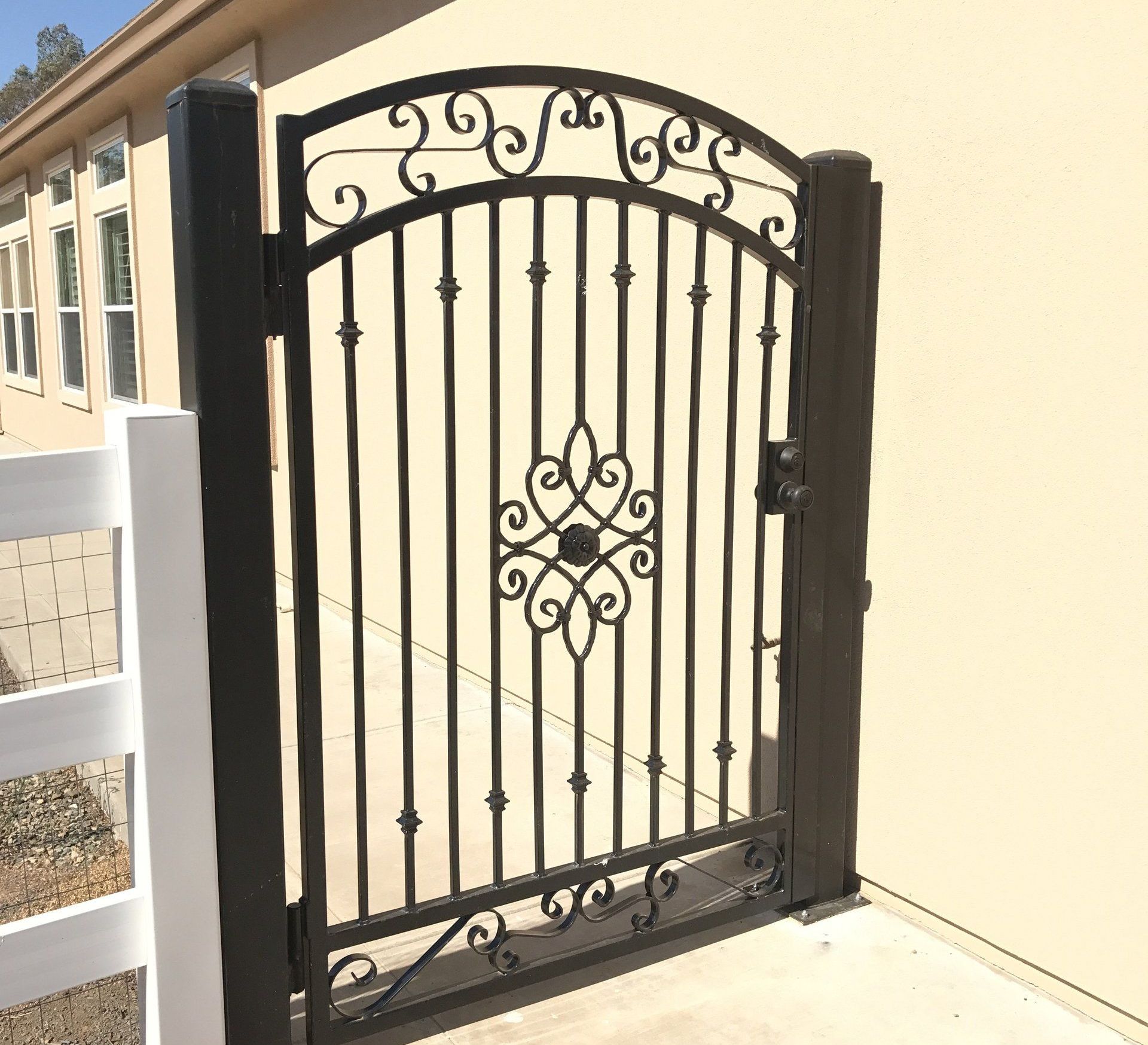 A black wrought iron gate with a white fence in front of a house.