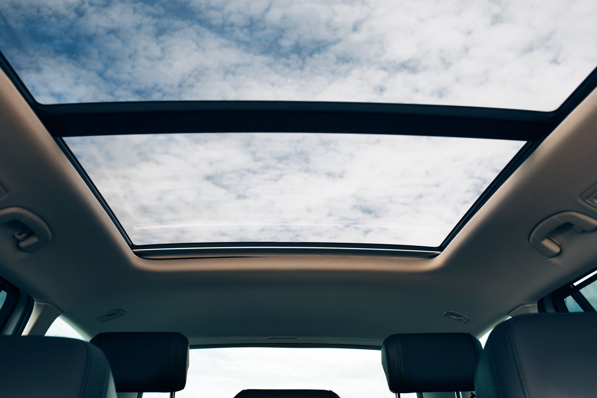 View from inside a car with an open sunroof; blue sky with clouds.
