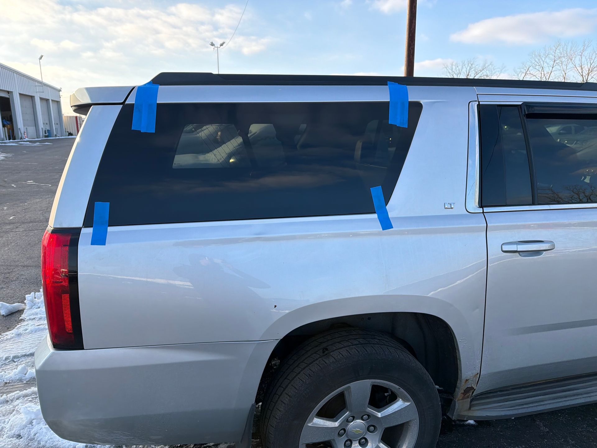 Silver SUV parked outdoors with blue tape marking damaged rear side window and body panel