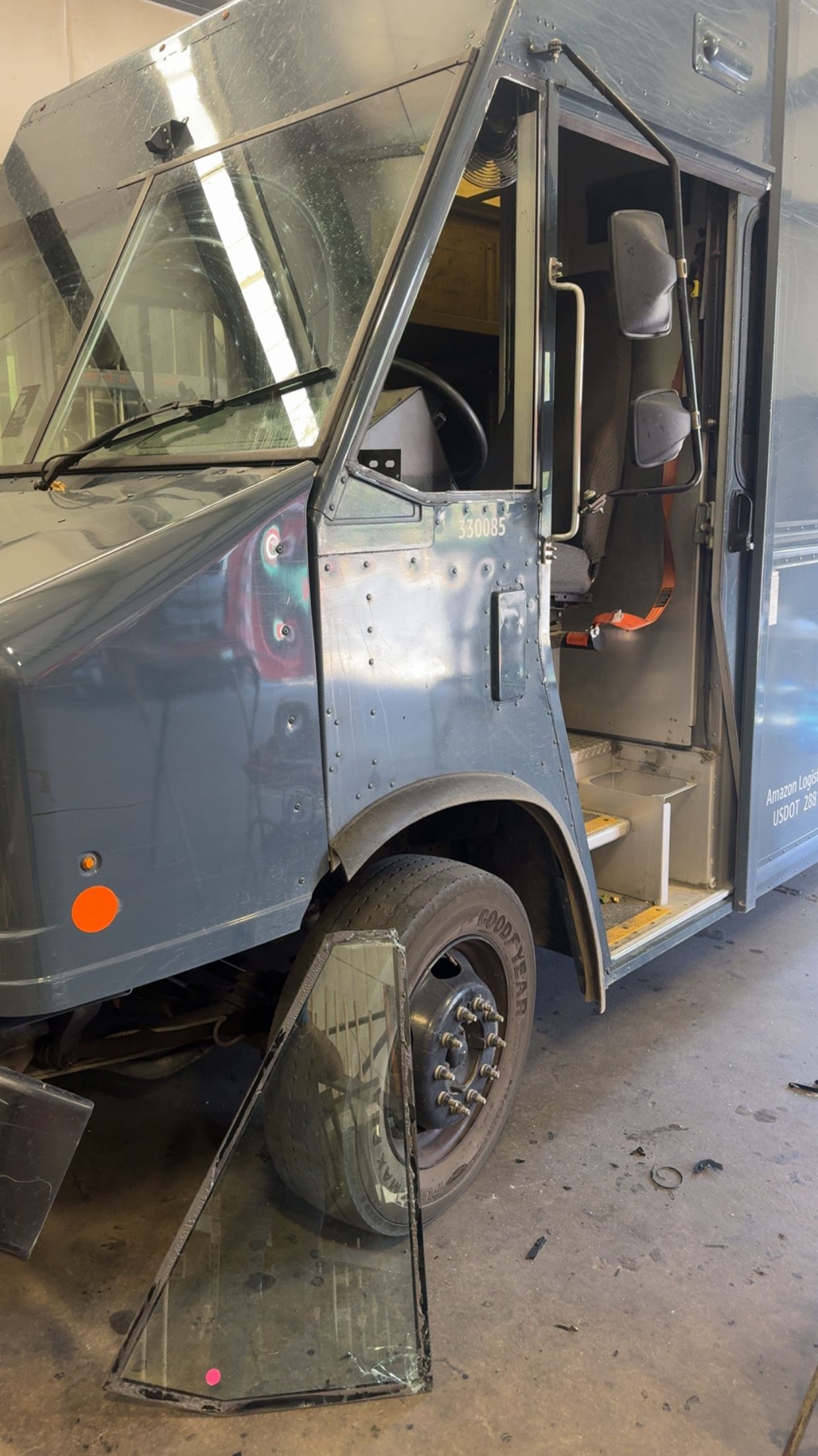 Damaged gray utility van with crumpled front end and open side door in a garage or workshop