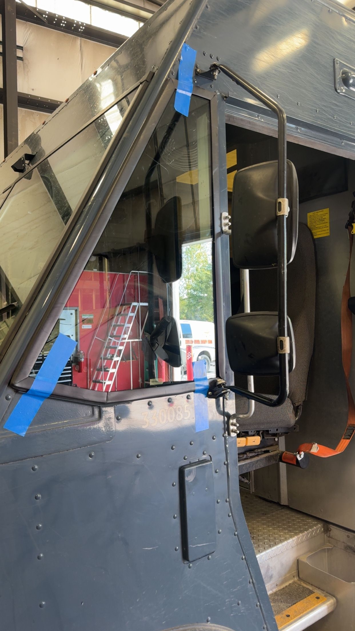Inside a train car, a blue-gray door and metal steps are shown with a handrail and a red sign in the background