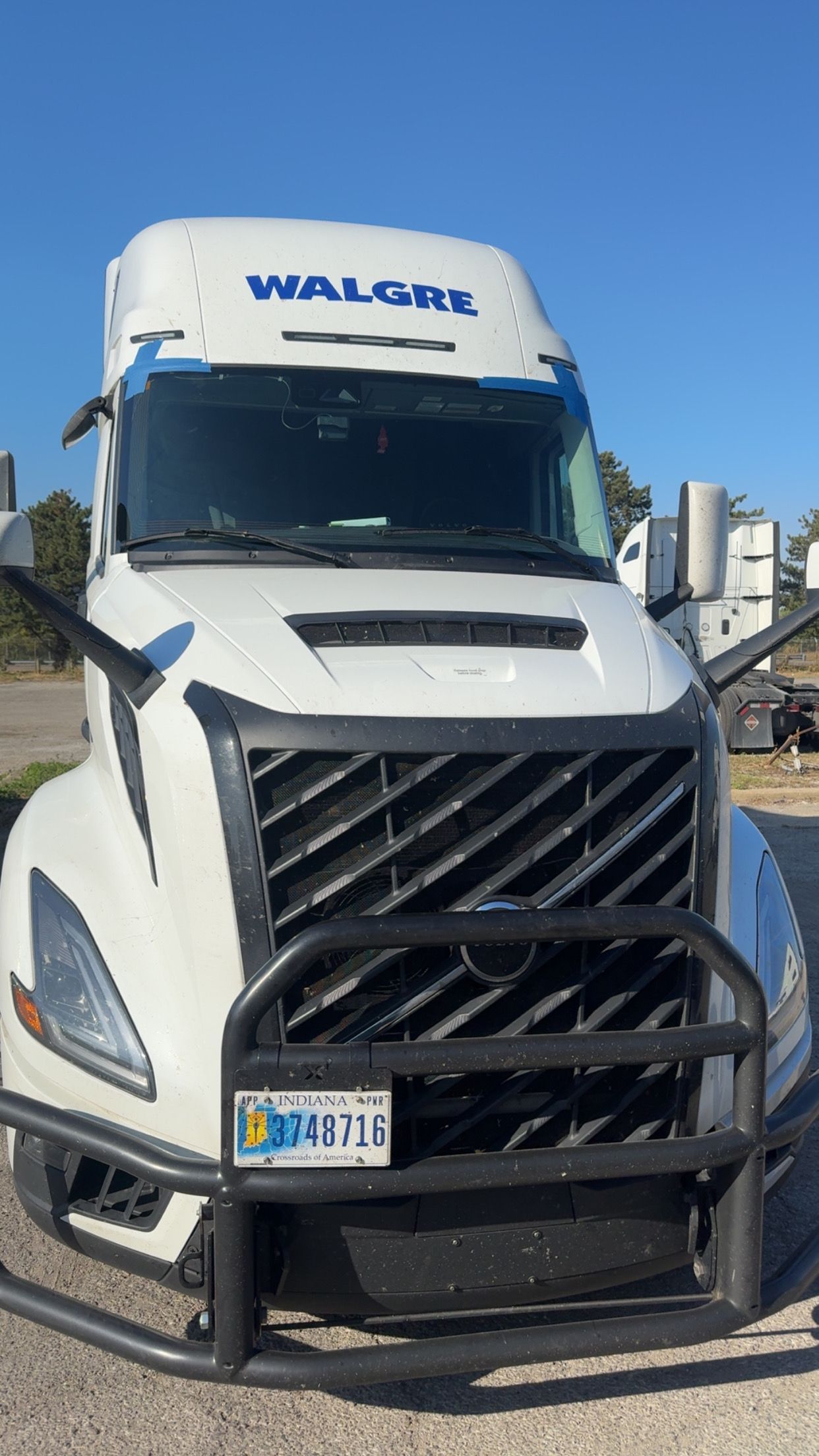 White semi-truck with a black grille guard parked outdoors on a sunny day.