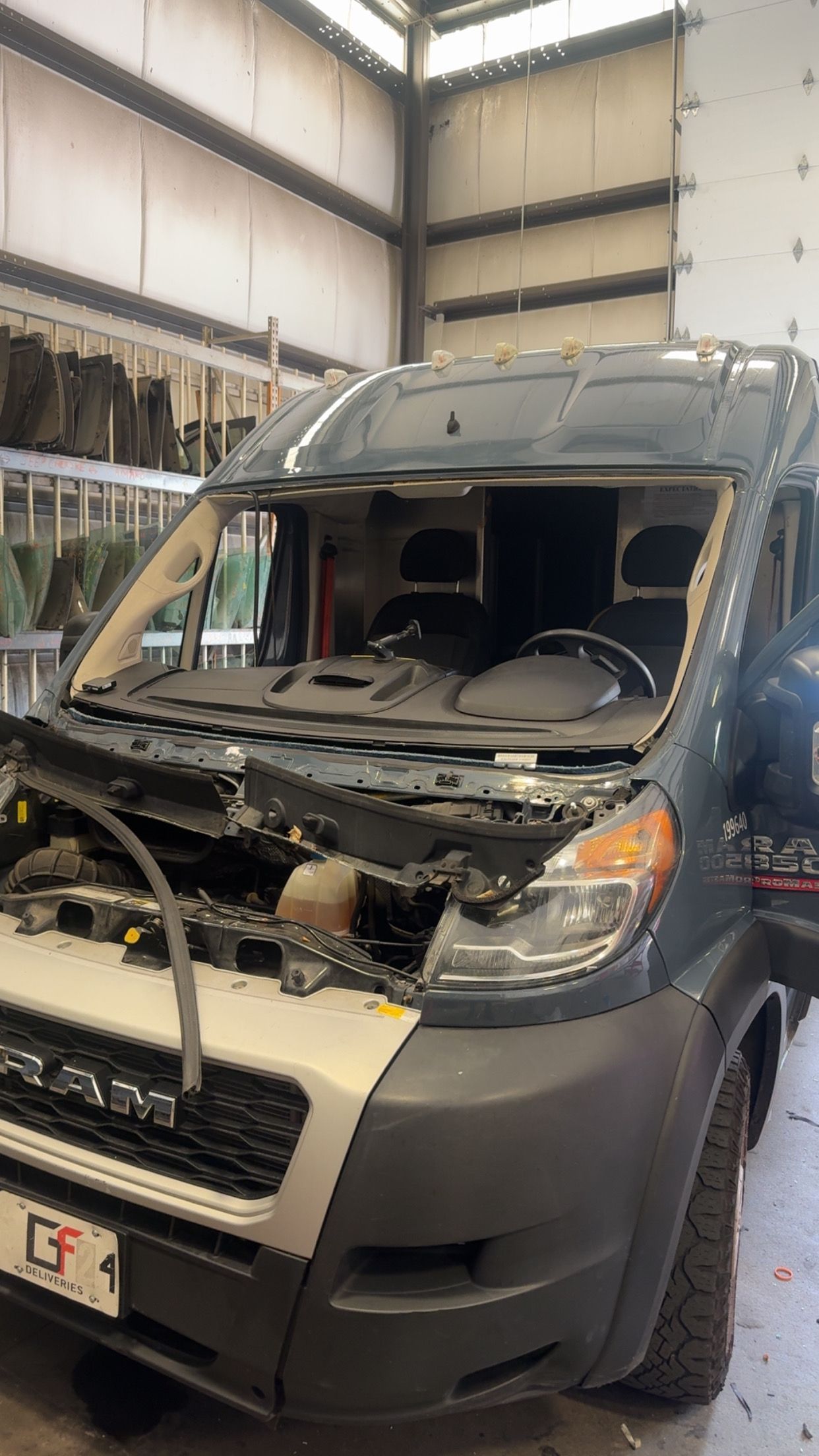 Damaged gray van with shattered windshield inside a repair shop after a collision