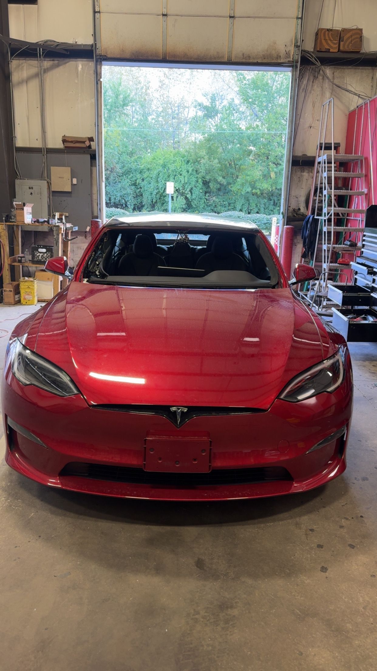 Red sports car parked inside a garage with an open door and greenery outside.