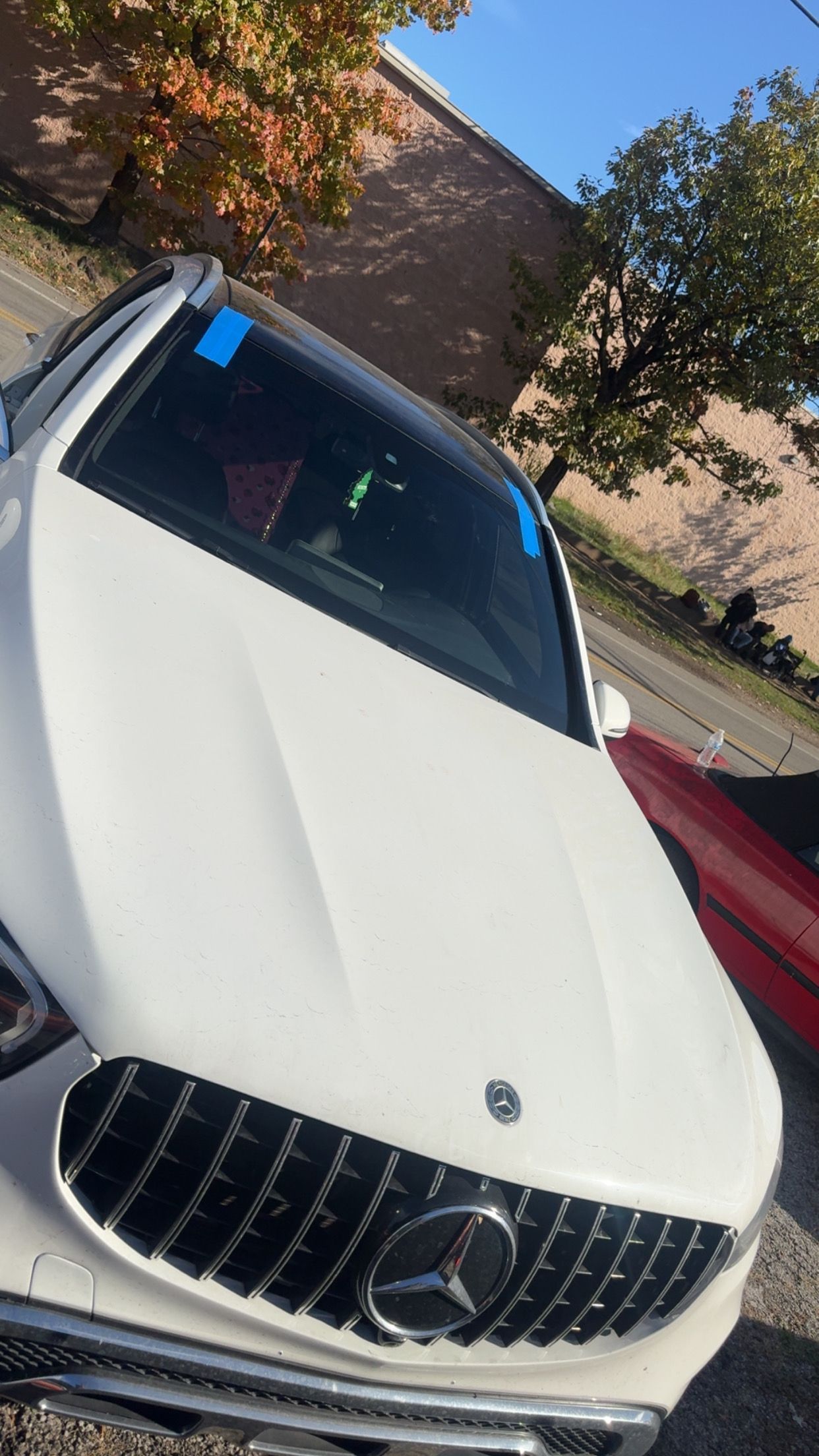 White Mercedes sedan parked outdoors beside a red car and trees, viewed at an angle.