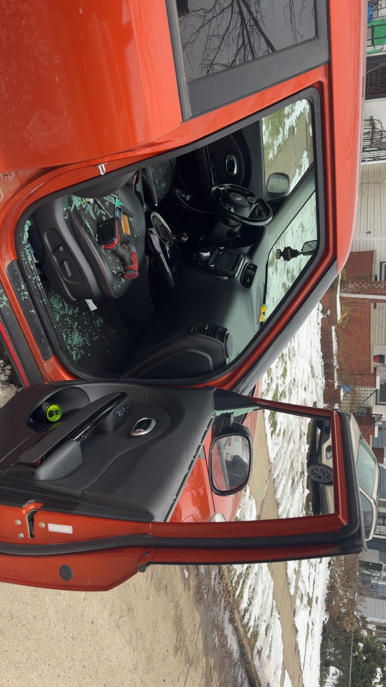 Orange car with open driver door, showing a black interior on a snowy roadside.