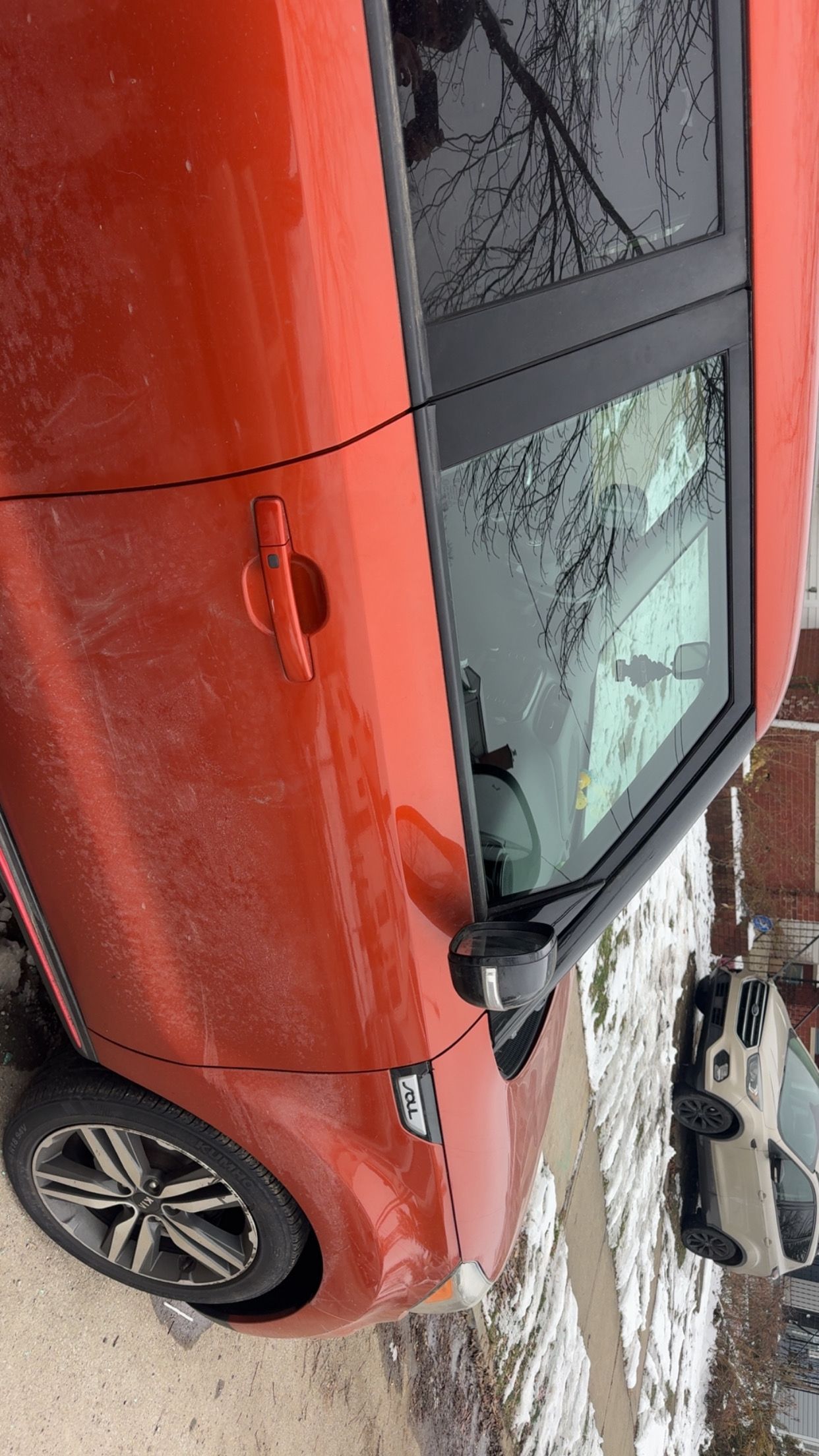 Red hatchback car parked on a snowy street, with frost on the windows.