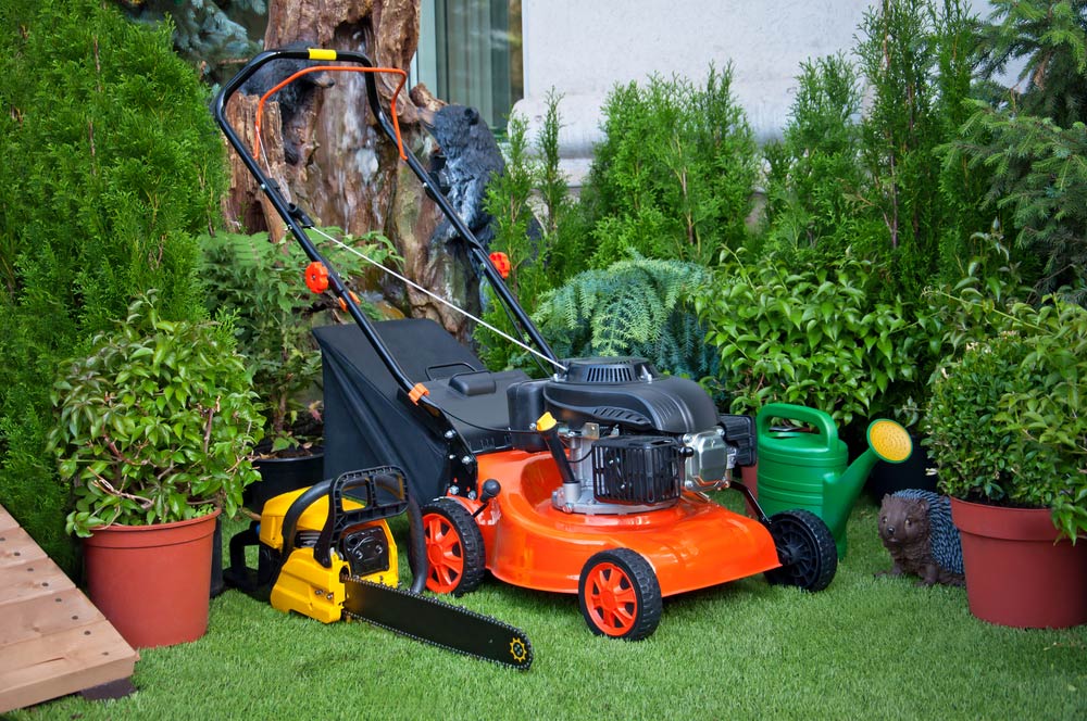A Lawn Mower, Chainsaw, and Watering Can Are Sitting on a Lush Green Lawn — Coffs Chainsaw and Mower in Kempsey, NSW