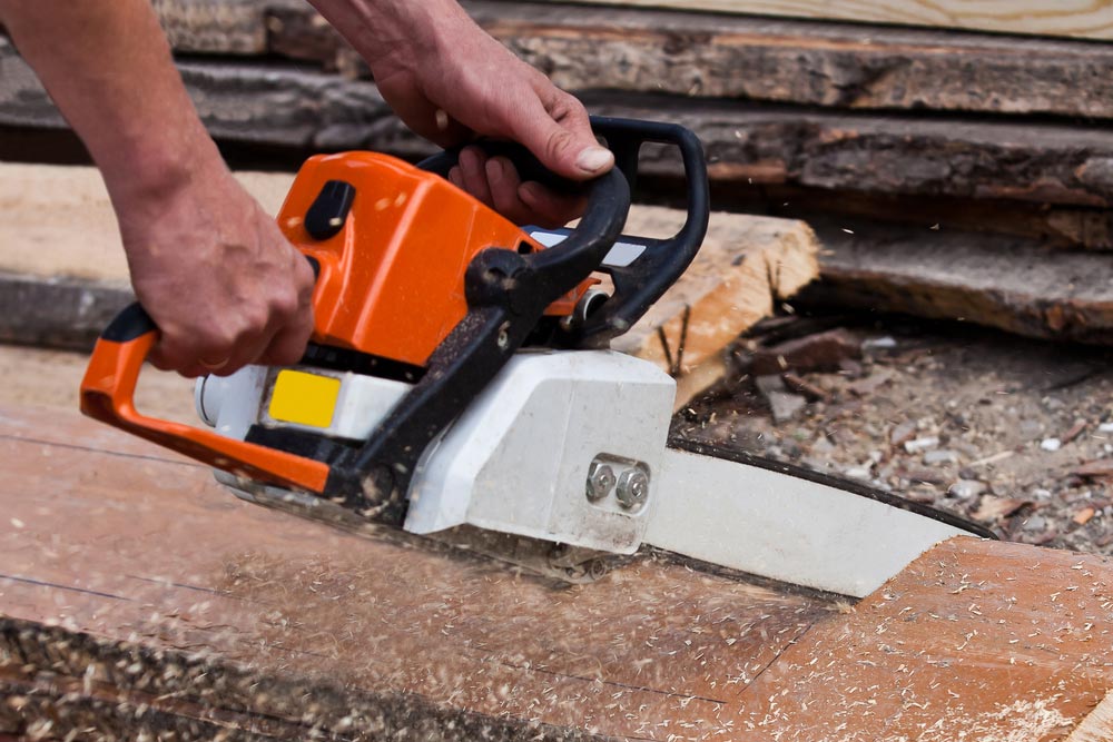 A Person is Using a Chainsaw to Cut a Piece of Wood — Coffs Chainsaw and Mower in Macksville, NSW