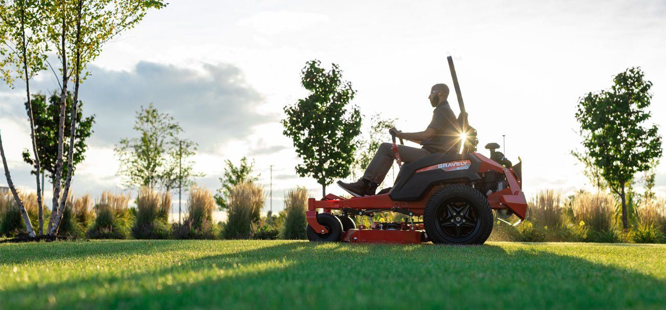 A Man is Riding a Lawn Mower on a Lush Green Lawn — Coffs Chainsaw and Mower in Bellingen, NSW