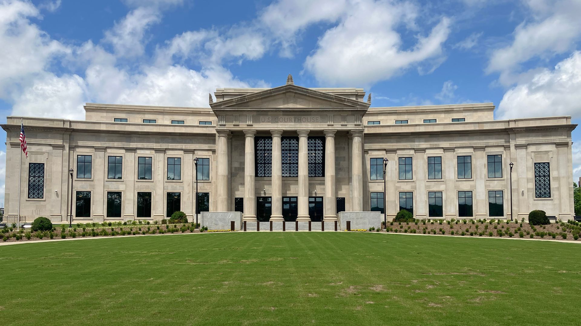 Neoclassical building with columns, windows, and a large lawn under a cloudy sky.
