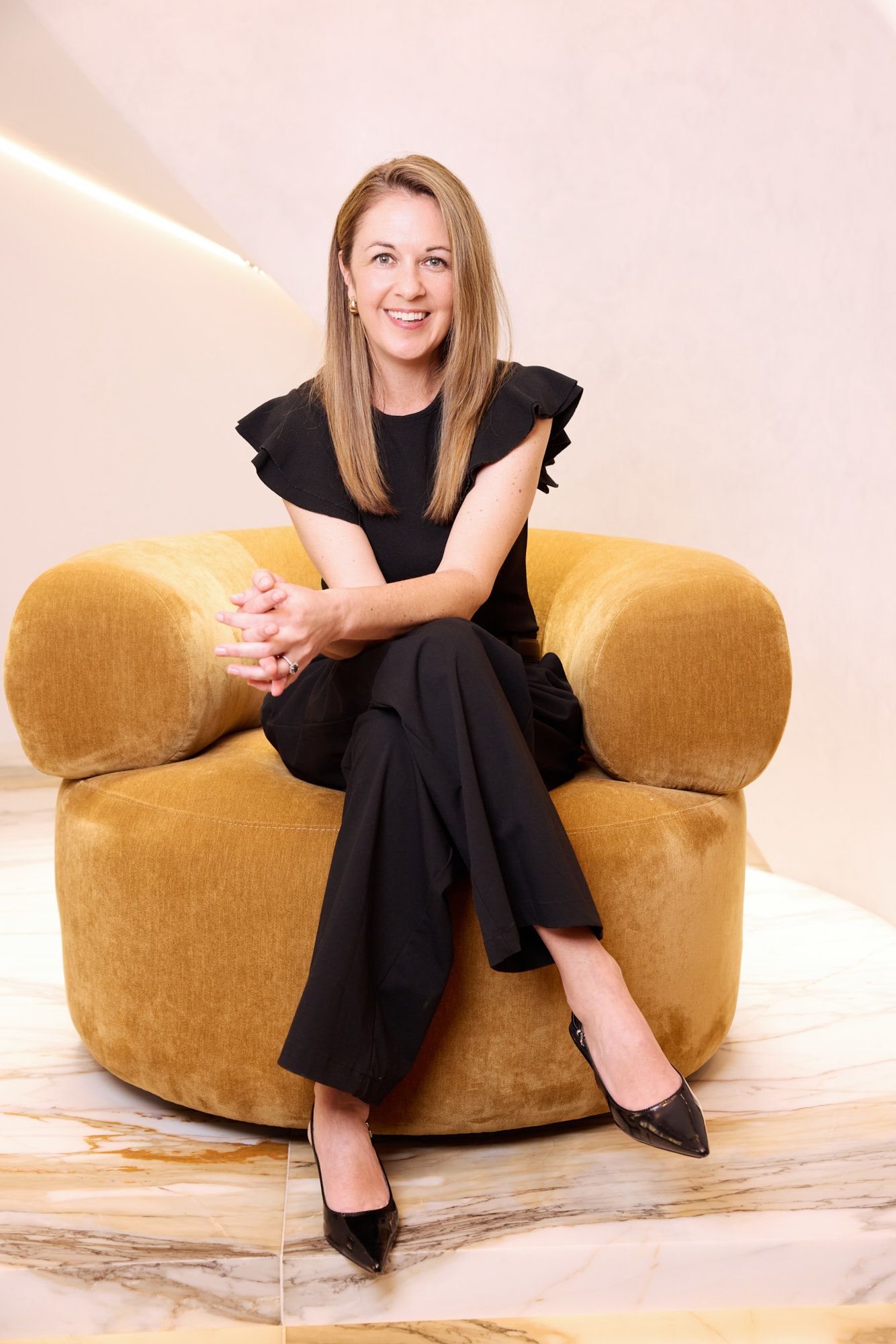 Smiling woman in a blazer standing in a bright office hallway with glass walls