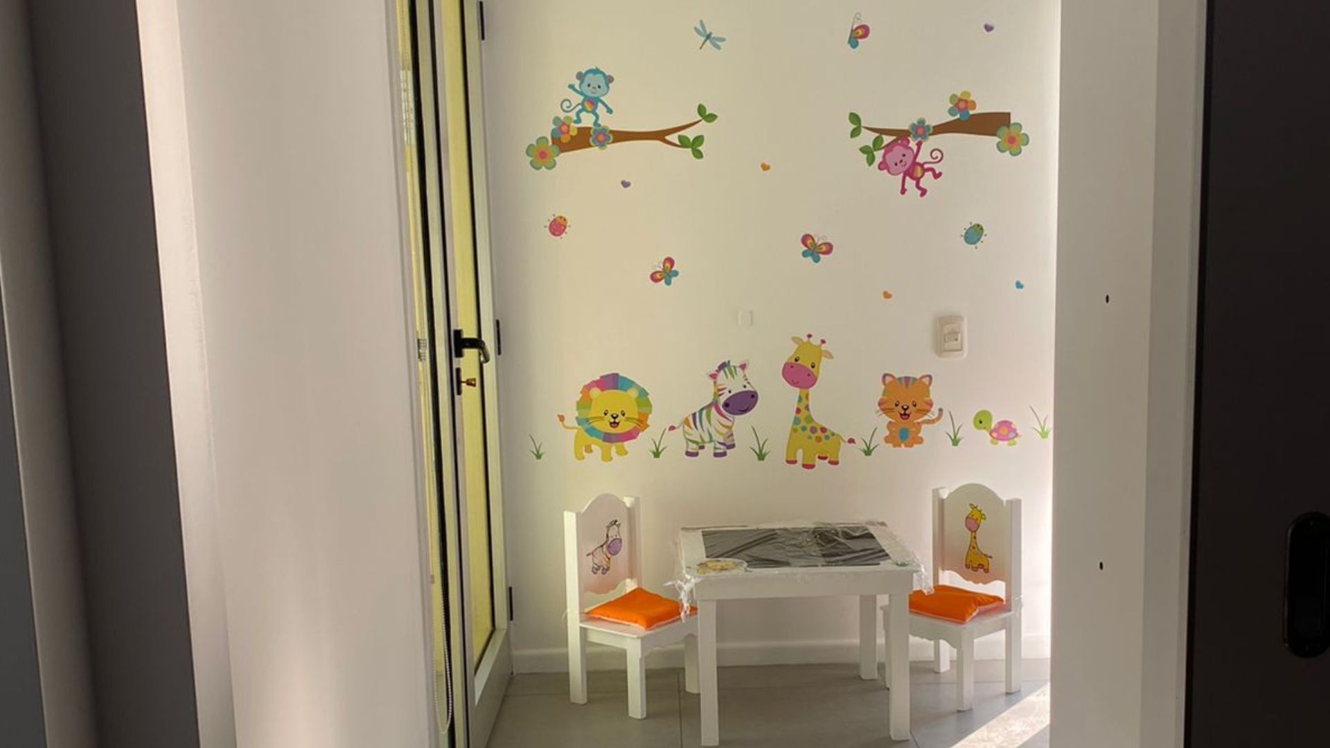Mesa y sillas blancas para niños bajo coloridos vinilos decorativos en un pequeño rincón de la sala de juegos.