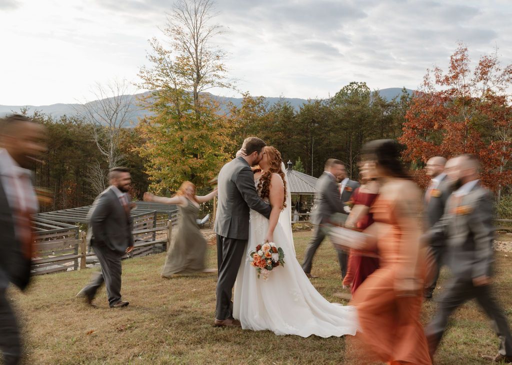 Bride and groom paused while guests walk by during outdoor wedding celebration with mountain views