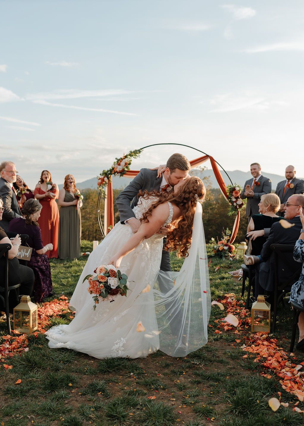 Bride and groom kissing beneath floral ceremony arch during Blue Ridge mountain wedding celebration