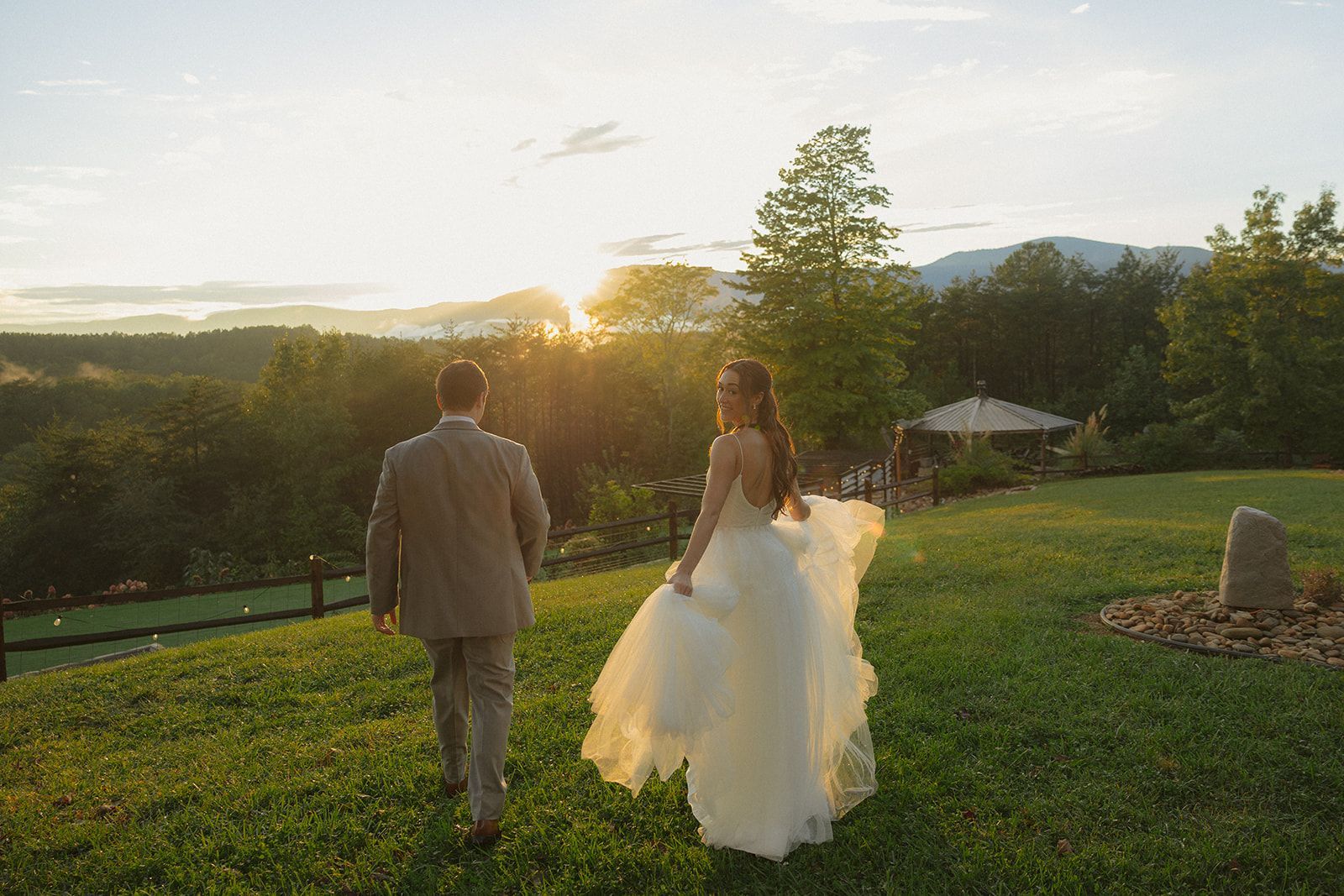 Bride and groom walking together at sunset across mountain lawn during wedding weekend in North Carolina