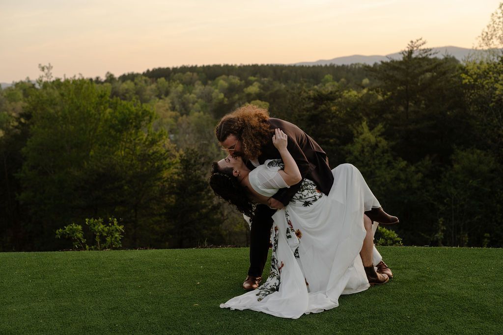 Bride and groom sharing playful sunset portrait on mountain lawn during wedding weekend celebration
