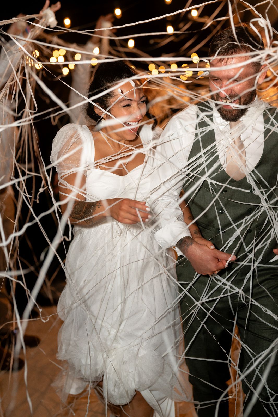 Bride and groom embracing beneath streamers and string lights during evening wedding celebration