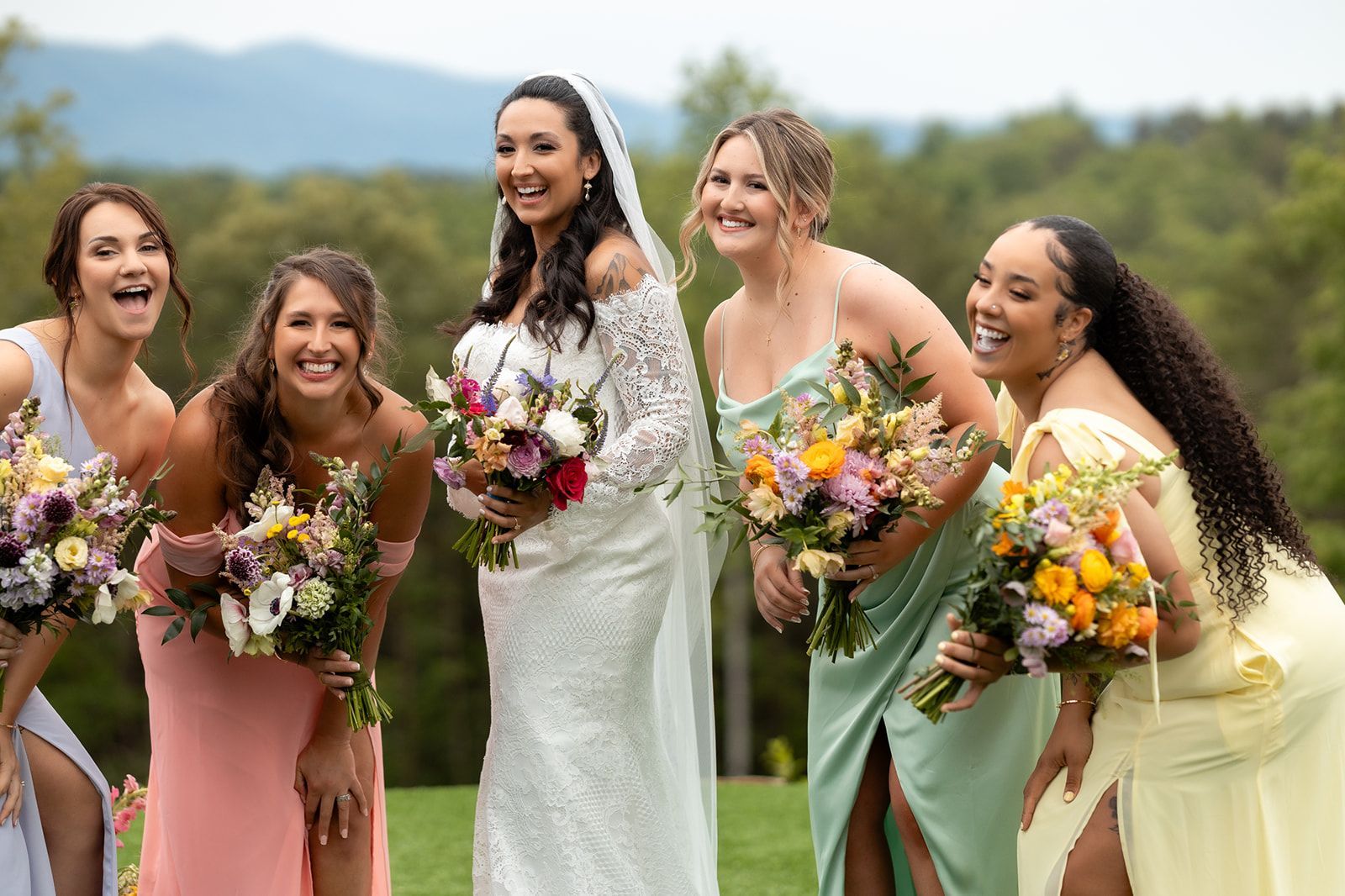 Bride and bridesmaids laughing together with colorful bouquets during outdoor wedding celebration