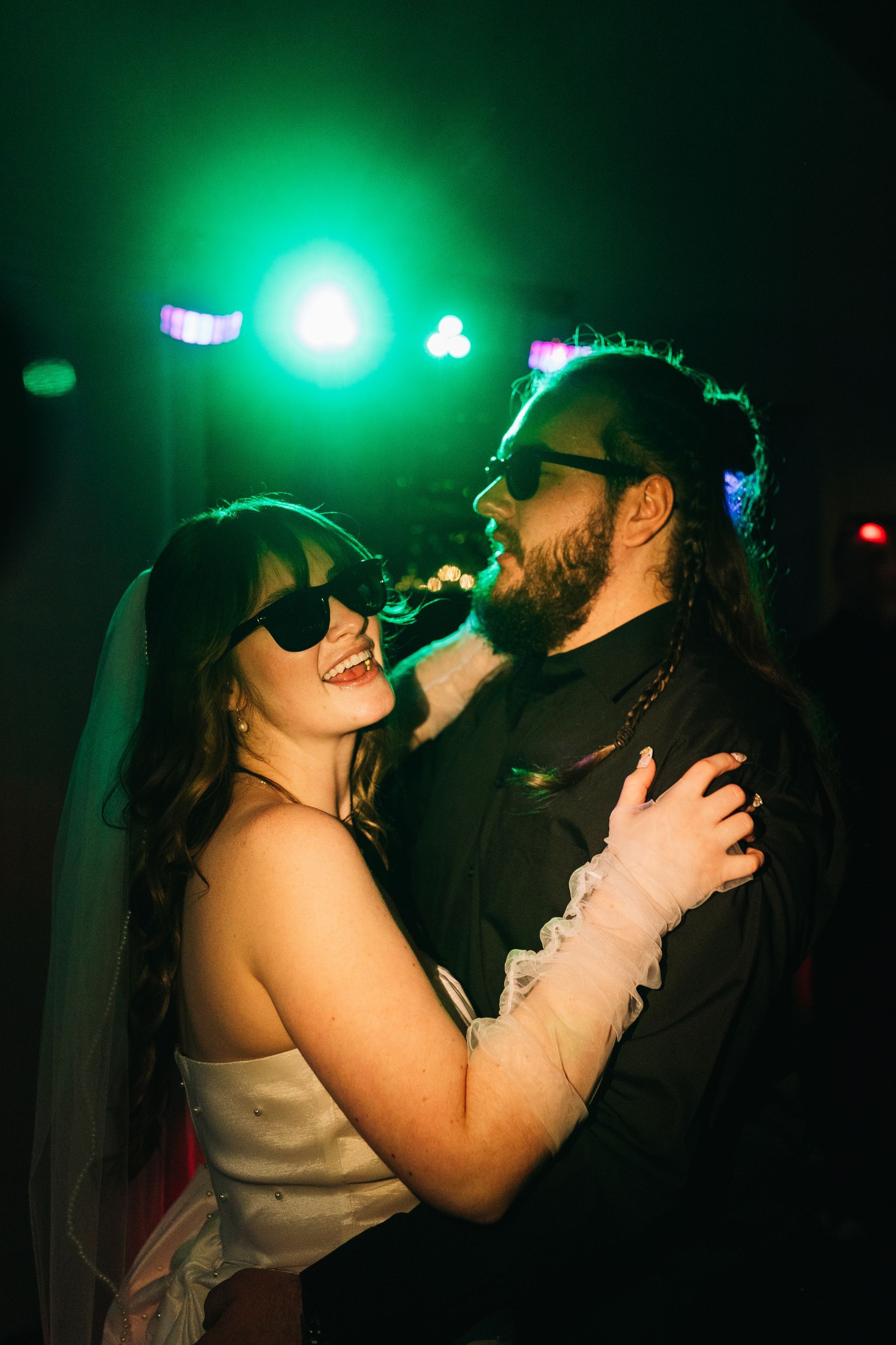 Couple dancing together during lively evening wedding reception with colorful lighting