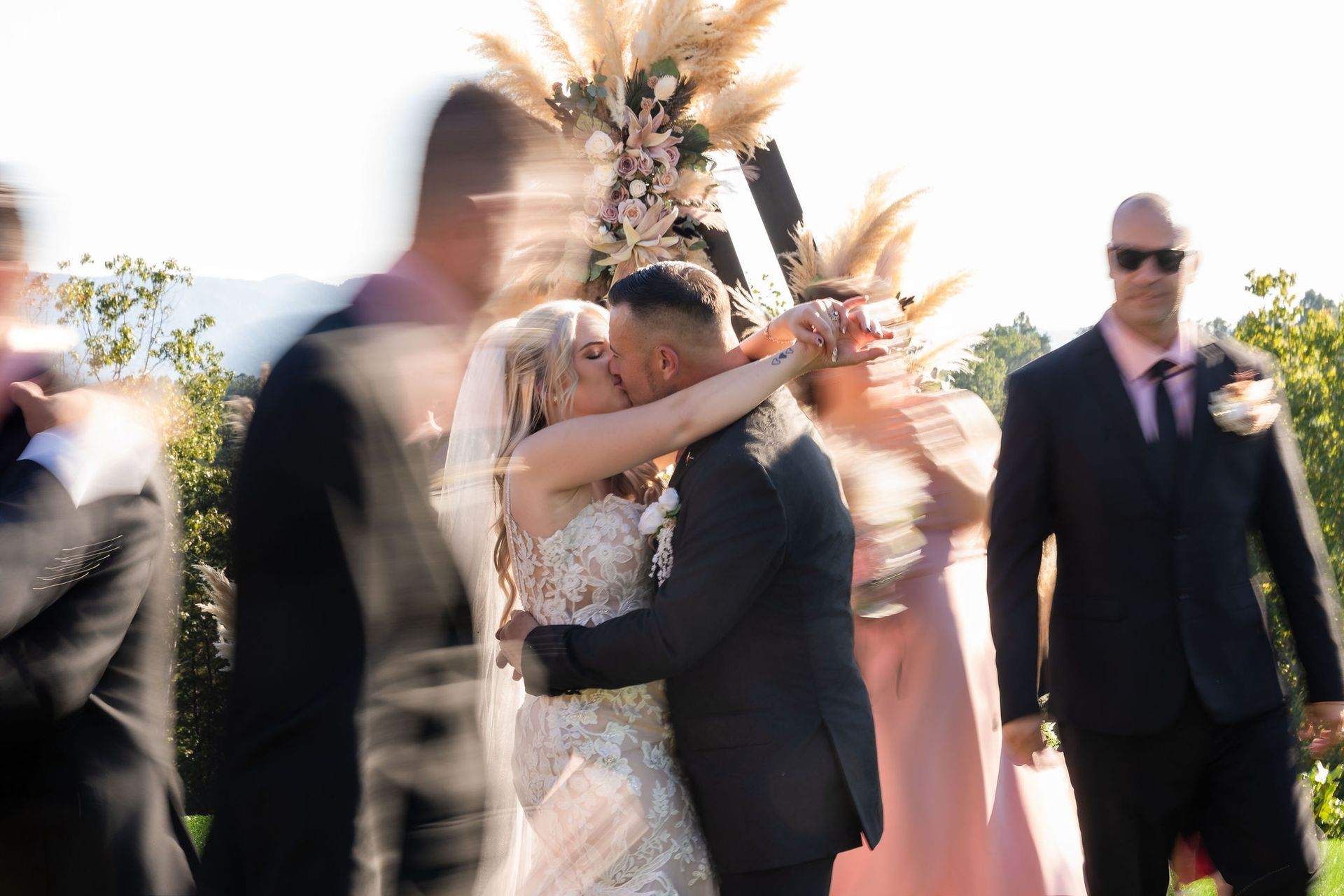 Bride and groom embracing during outdoor wedding ceremony with guests gathered in mountain setting