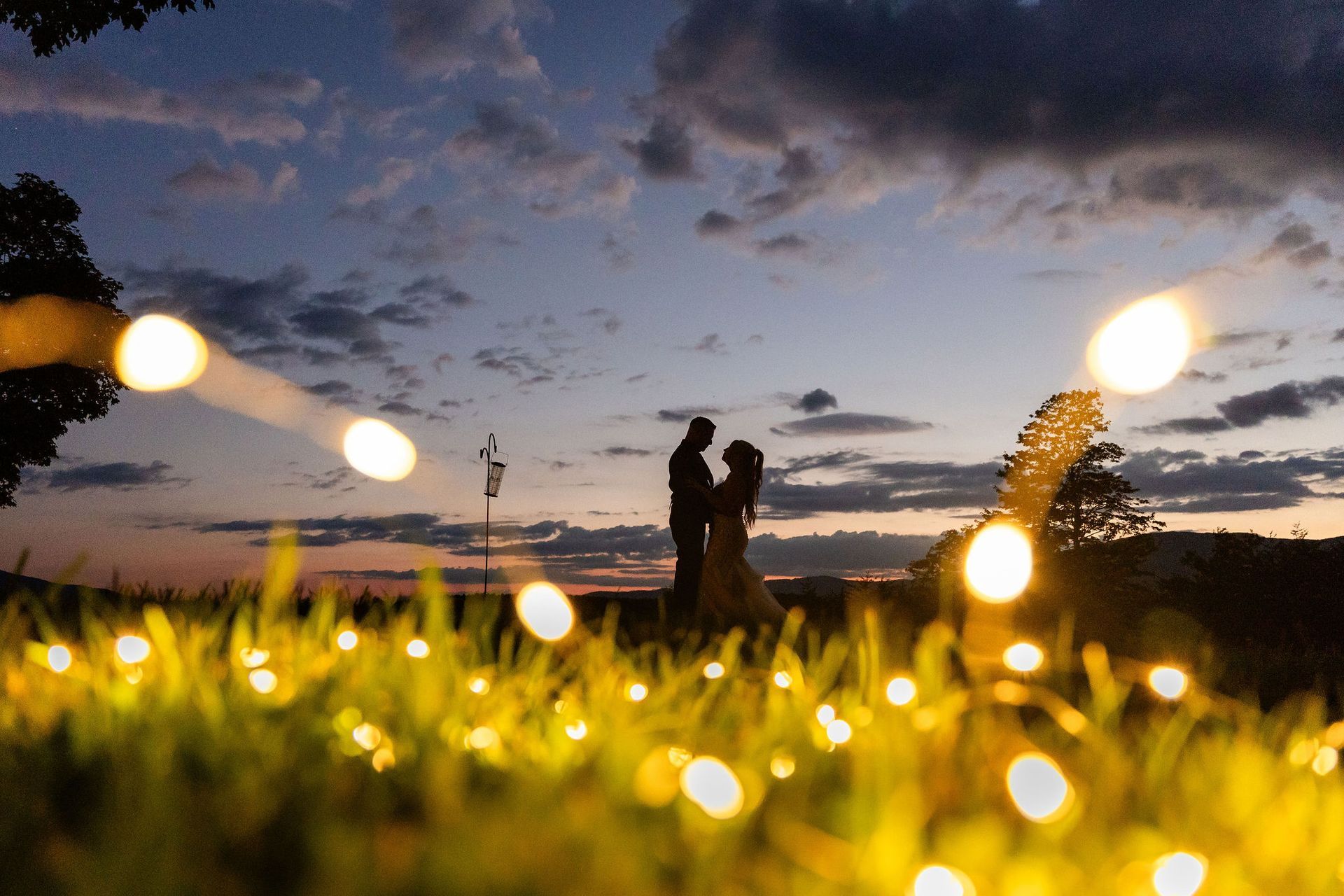 Couple silhouetted at dusk with glowing lights during romantic mountain wedding evening