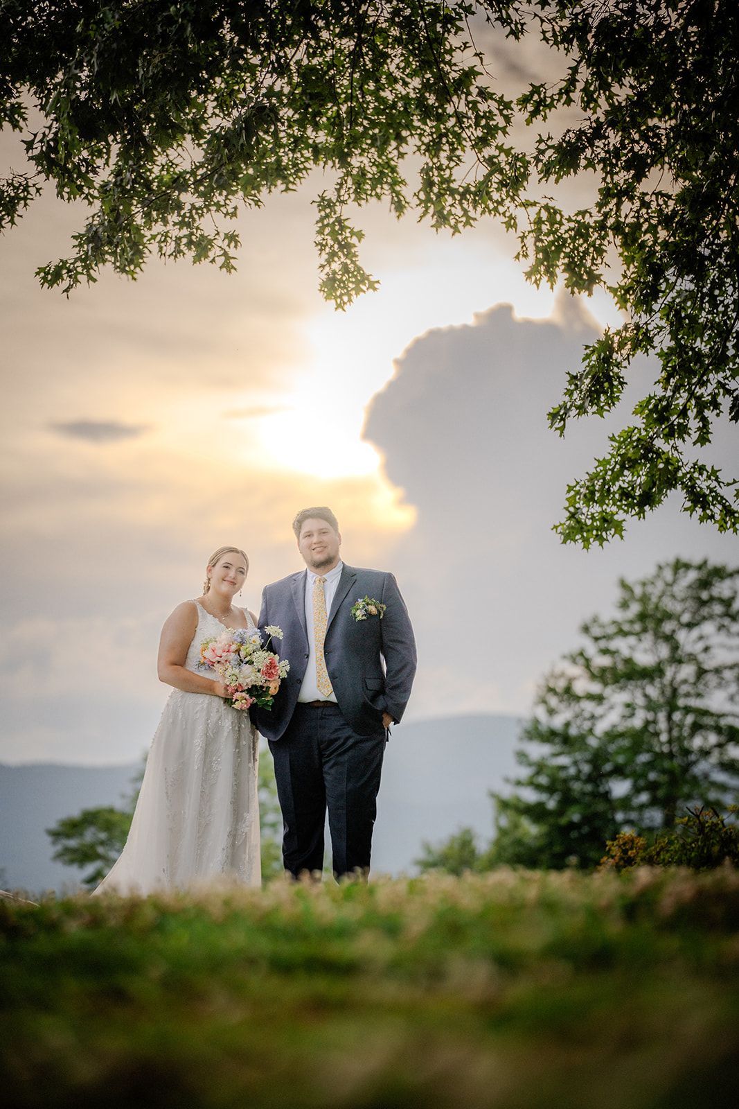 Newlyweds posing beneath tree canopy with mountain sunset glow at outdoor wedding venue