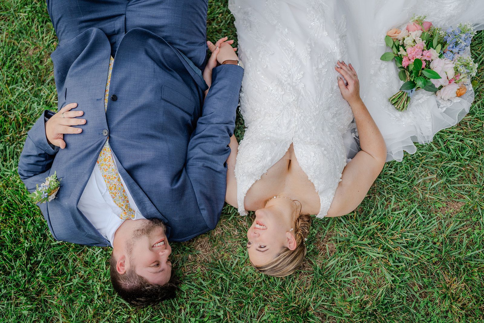 Bride and groom lying together on grass during playful wedding portrait session in western North Carolina