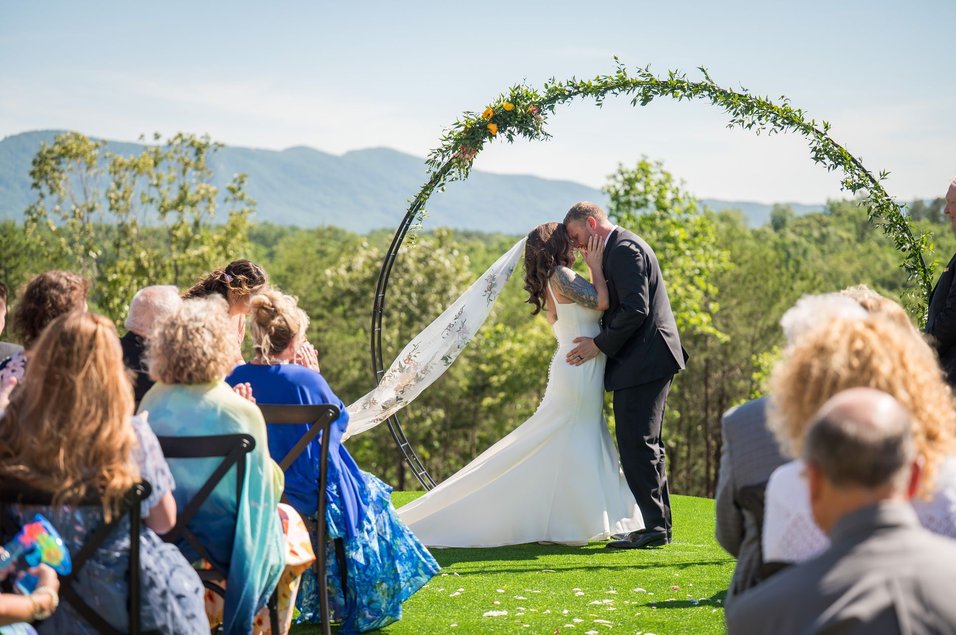 Bride and groom kissing beneath floral ceremony arch with mountain backdrop in North Carolina