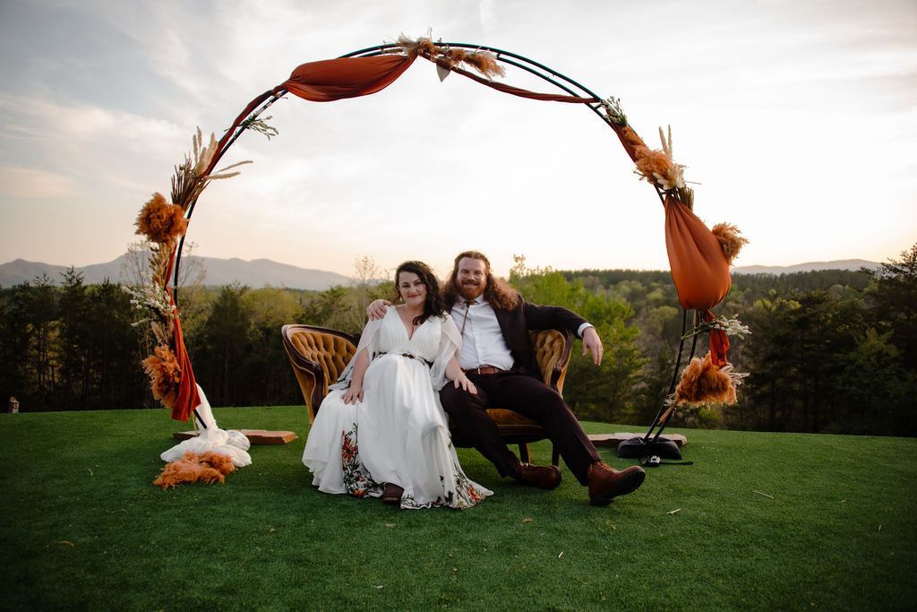 Bride and groom relaxing beneath floral ceremony arch at scenic mountain wedding venue