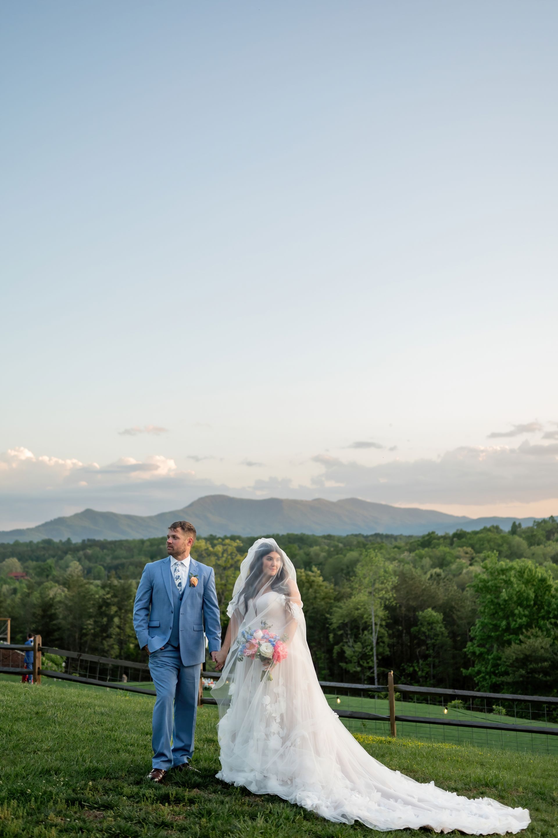 Bride and groom posing on mountain overlook with flowing veil during destination wedding weekend