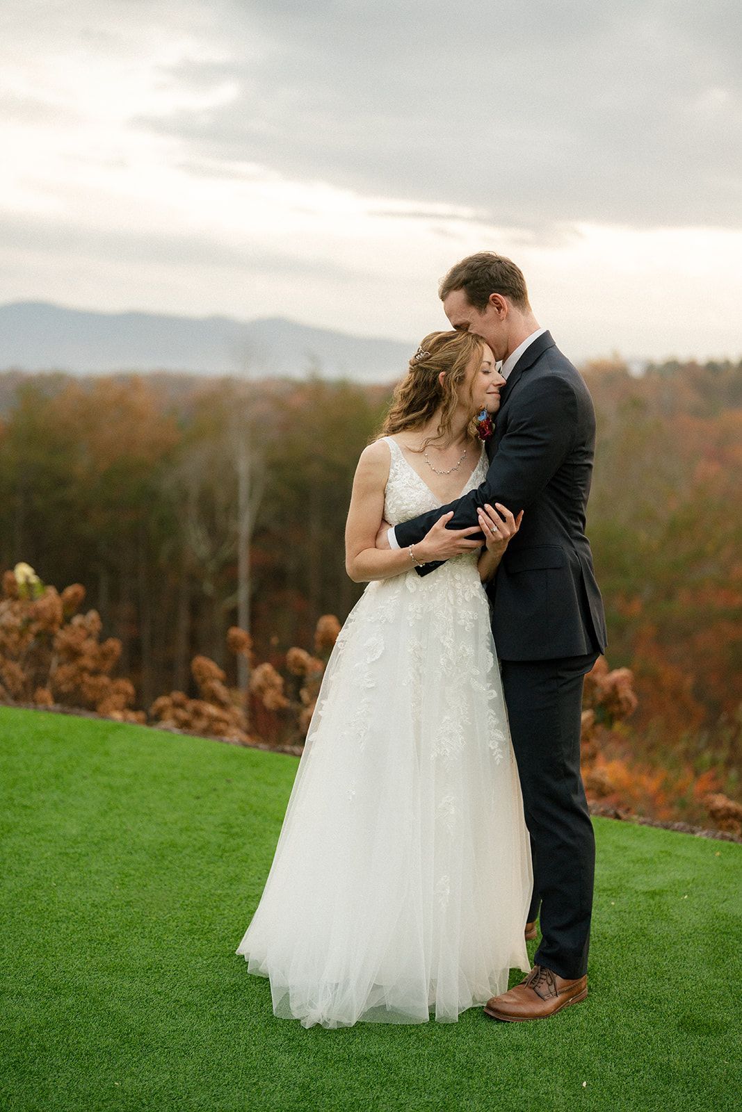 Newlyweds embracing on ceremony lawn with Blue Ridge mountain views at WNC wedding venue