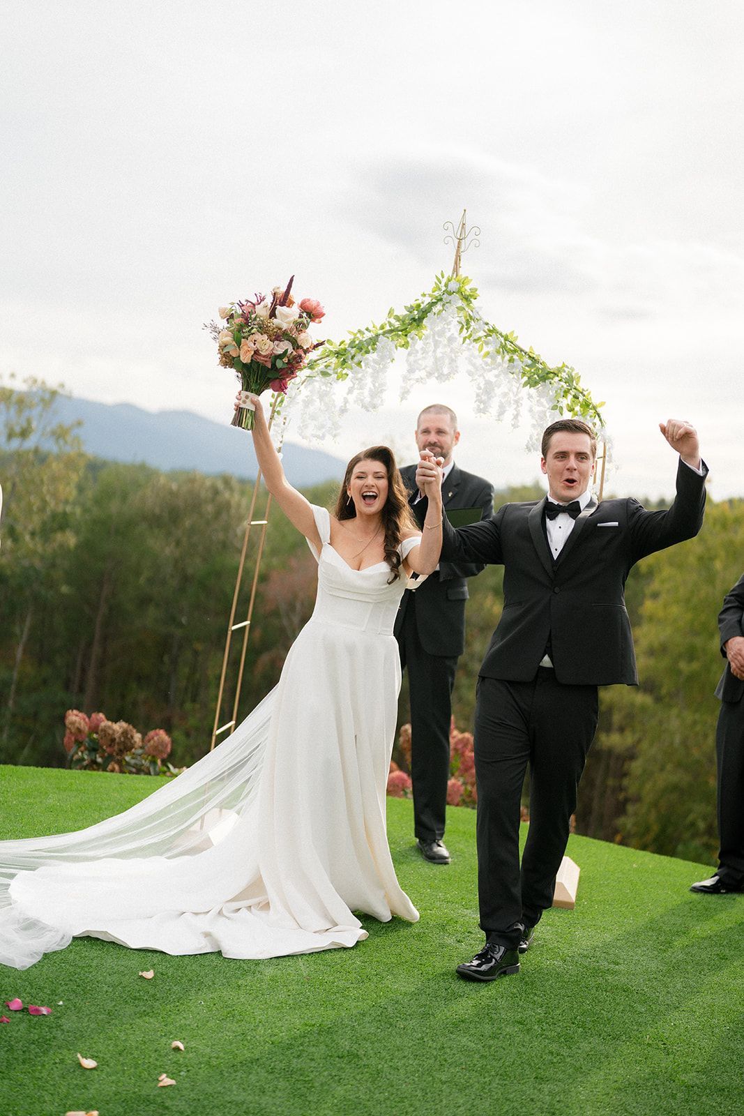 Newlyweds celebrating their ceremony exit beneath floral arch at outdoor mountain wedding venue