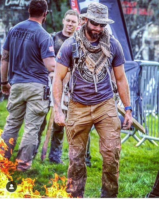 A man in a hat and scarf is standing in front of a fire