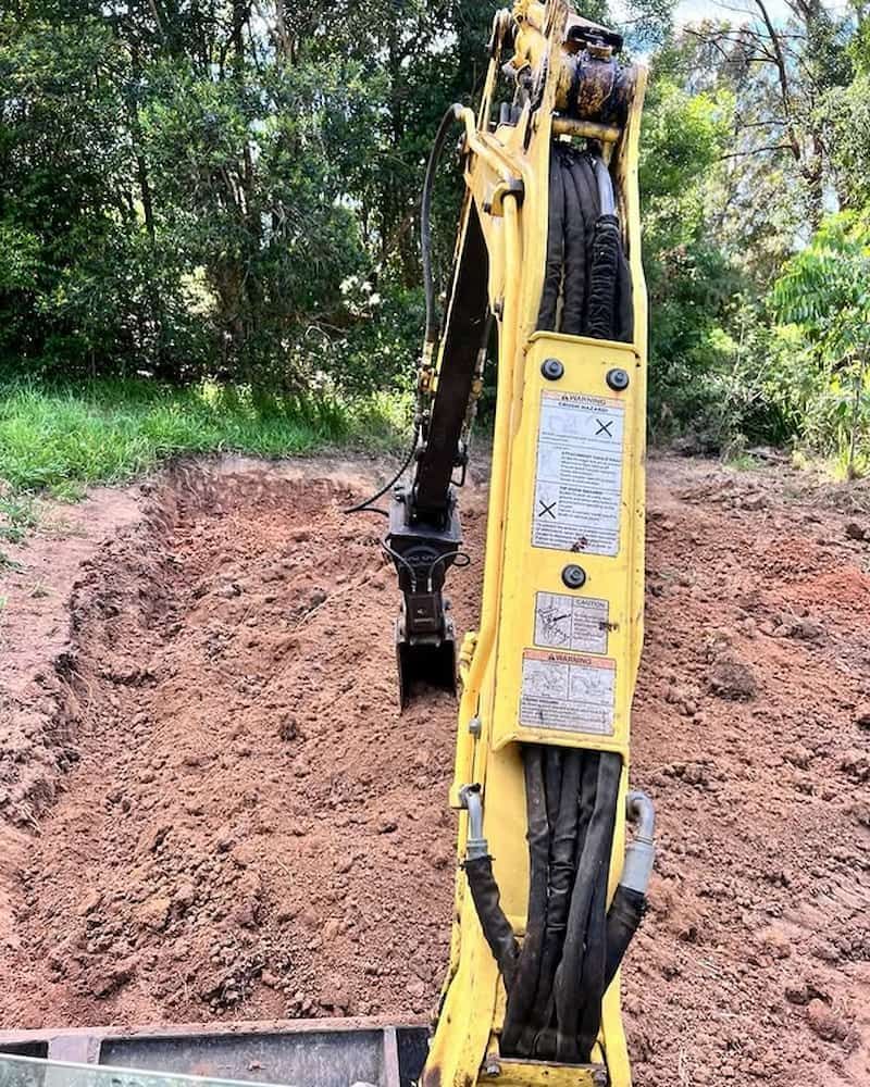 Yellow Excavator Digging Into a Muddy Bank, in a Wooded Area — Heller Excavation & Tree Services in Mullumbimby, NSW