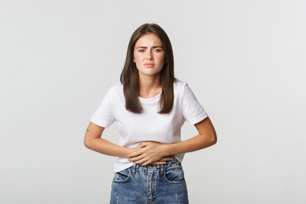 A young woman is holding her stomach in pain.
