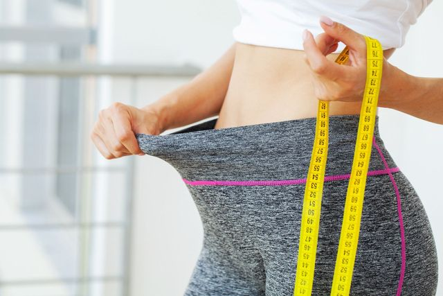 A woman is measuring her waist with a tape measure.
