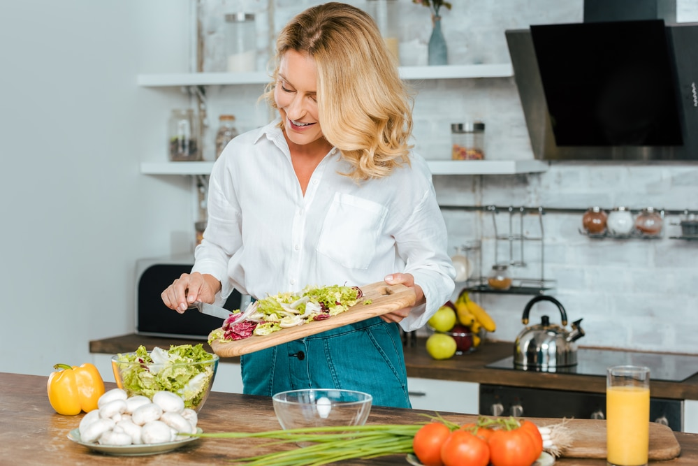 A woman is cutting vegetables on a cutting board in a kitchen.