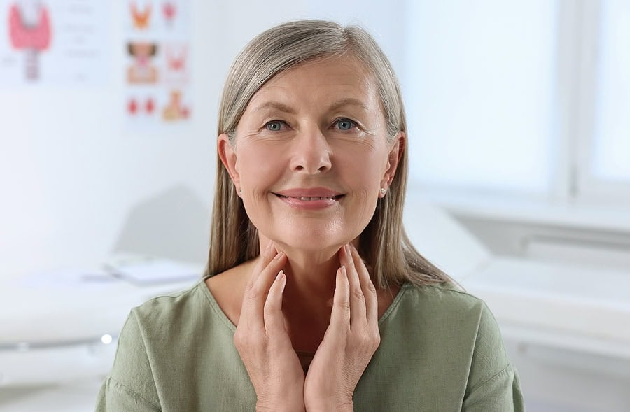An older woman is smiling and touching her neck.