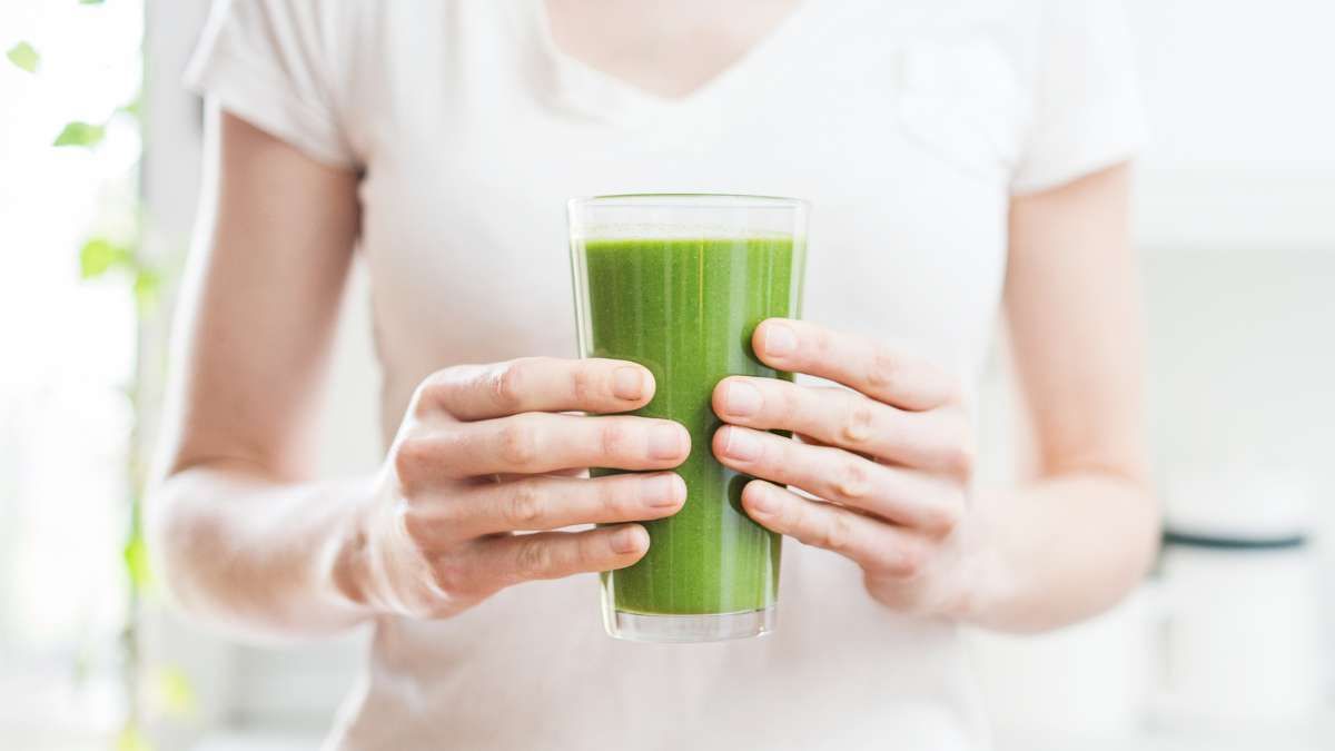 A woman is holding a glass of green juice in her hands.