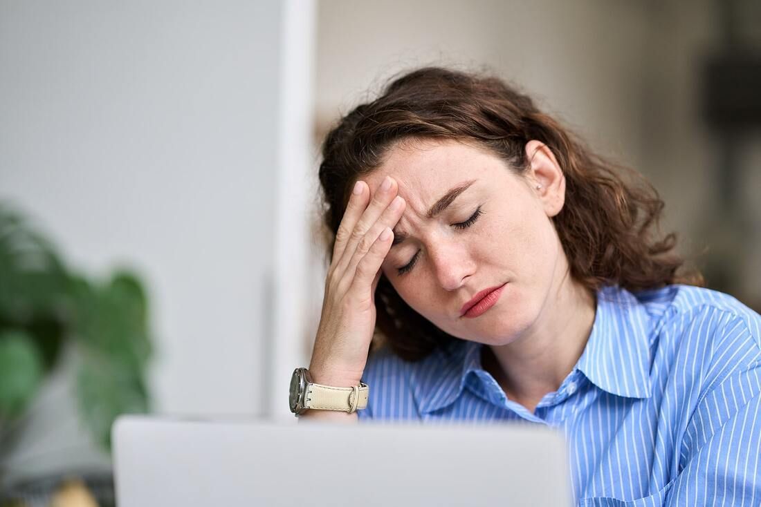 A woman is sitting in front of a laptop computer with her hand on her forehead.